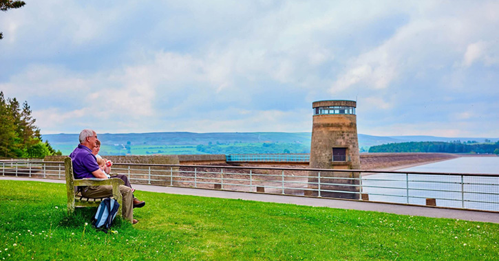 grandparents and grandchild sit on beach admiring view of Derwent Reservoir 